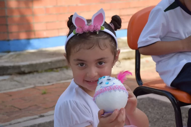 Niña de preescolar con diadema de orejas de conejo muestra un huevo decorado.