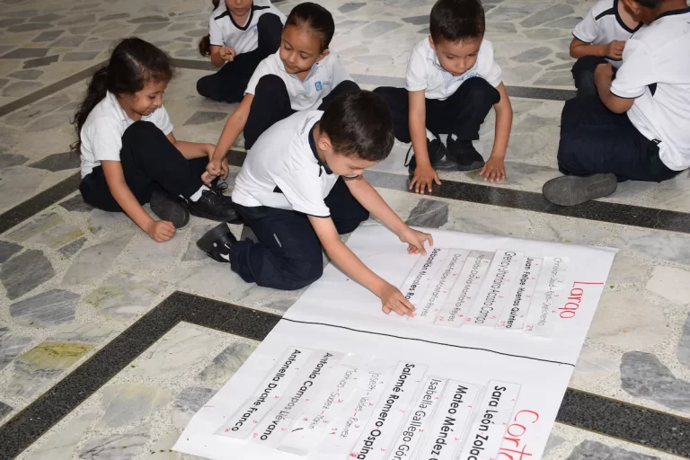 Niños de primaria, sentados en el piso, ordenan tarjetas con nombres sobre un pliego de papel.