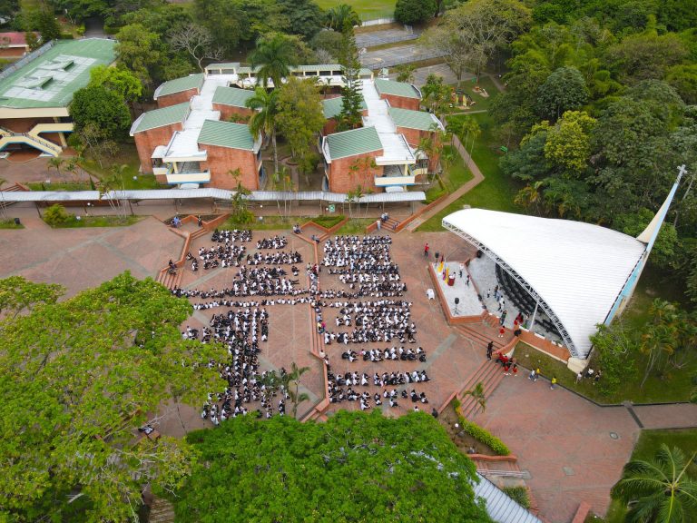 Vista aérea del campus, con sus edificios, zonas verdes y estudiantes reunidos en la plaza.